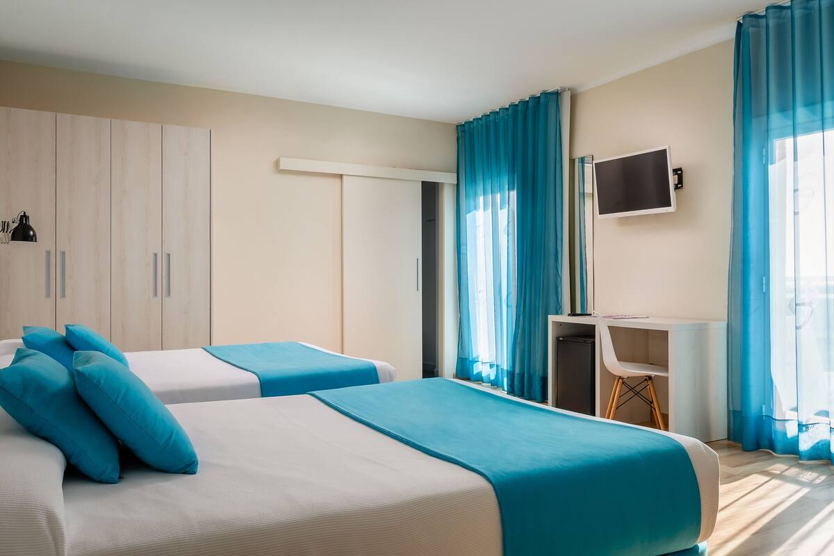 Una habitación de hotel con dos camas, un escritorio, un televisor y un armario.