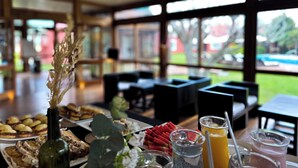 A breakfast buffet with various dishes, a bottle, and drinks on a table in a room with large windows and a view of the outdoors. - Casa del Sol (Colonia del Sacramento)