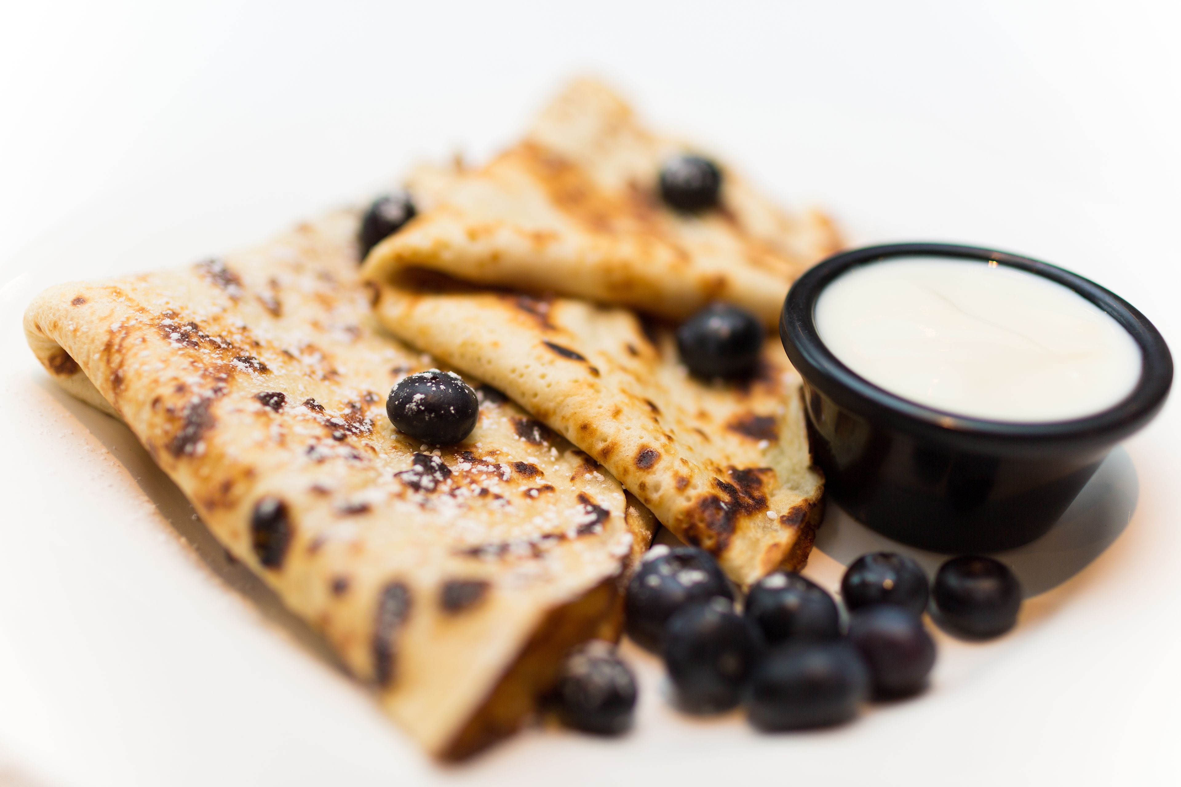 Crepas con arándanos y un tazón pequeño de crema.