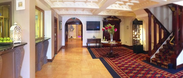 Un vestíbulo de hotel con piso de madera, alfombra roja, una escalera y un letrero que indica la ubicación de un centro de negocios.