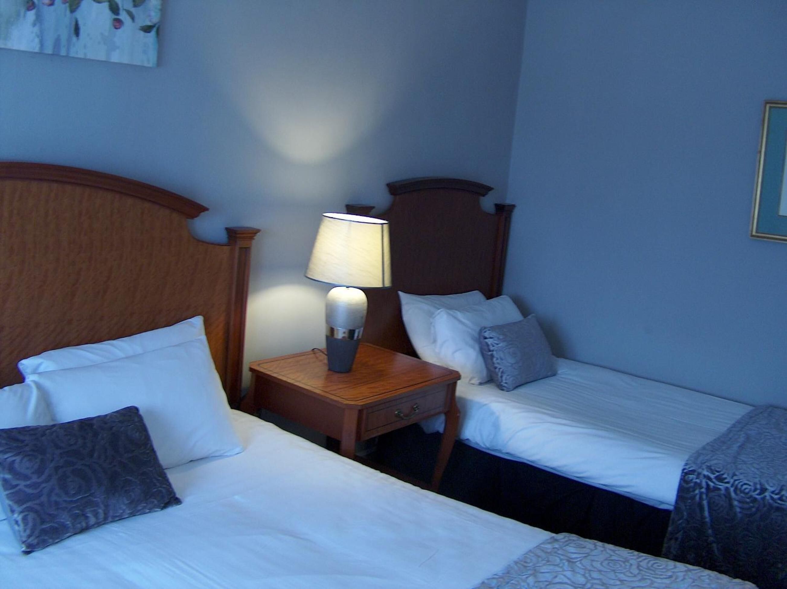 Une chambre d’hôtel avec deux lits simples, une table de chevet avec une lampe et une tête de lit en bois.