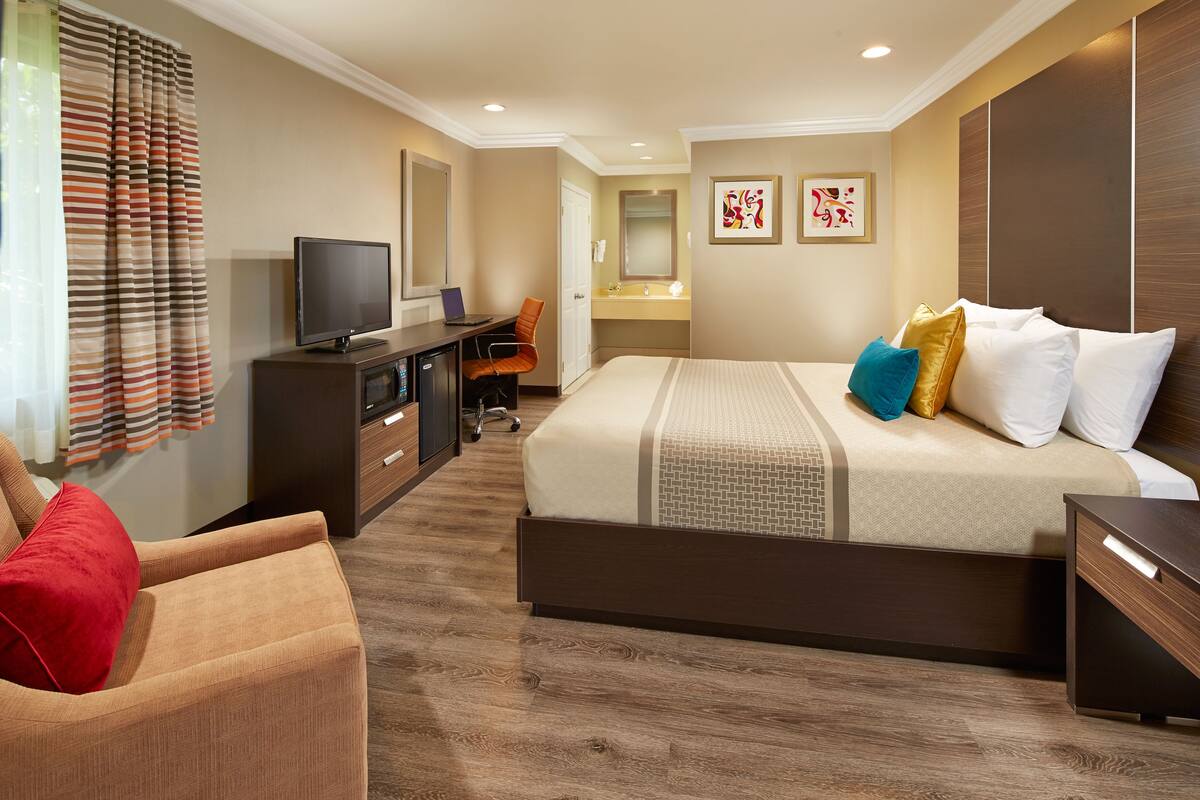 Une chambre d’hôtel avec un grand lit, un bureau avec une télévision, une chaise, une armoire et une salle de bain visible à travers une porte ouverte.