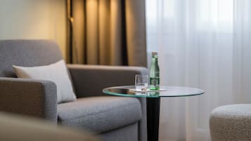 A modern living room with a grey sofa, a glass table with a bottle and glass, and a lamp in the background.
