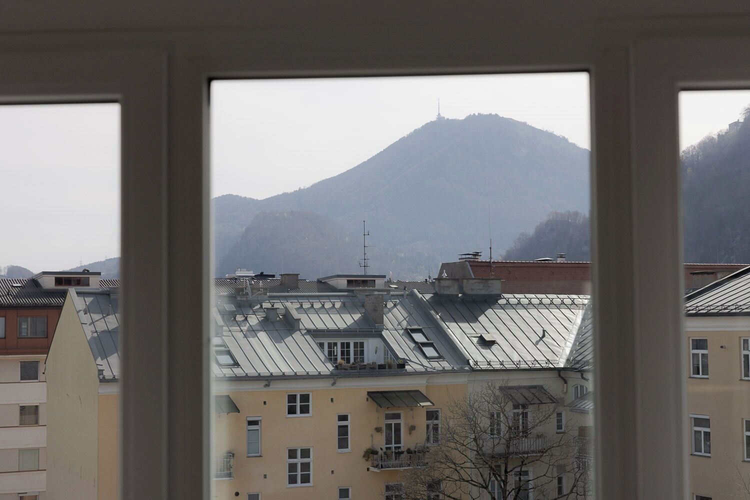 Une vue à travers la fenêtre d’un immeuble à plusieurs étages, avec une montagne en arrière-plan.