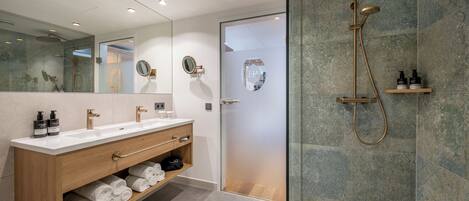 Un baño moderno con ducha envuelta en vidrio, tocador de madera con estante incorporado para toallas y un espejo grande sobre el lavabo.