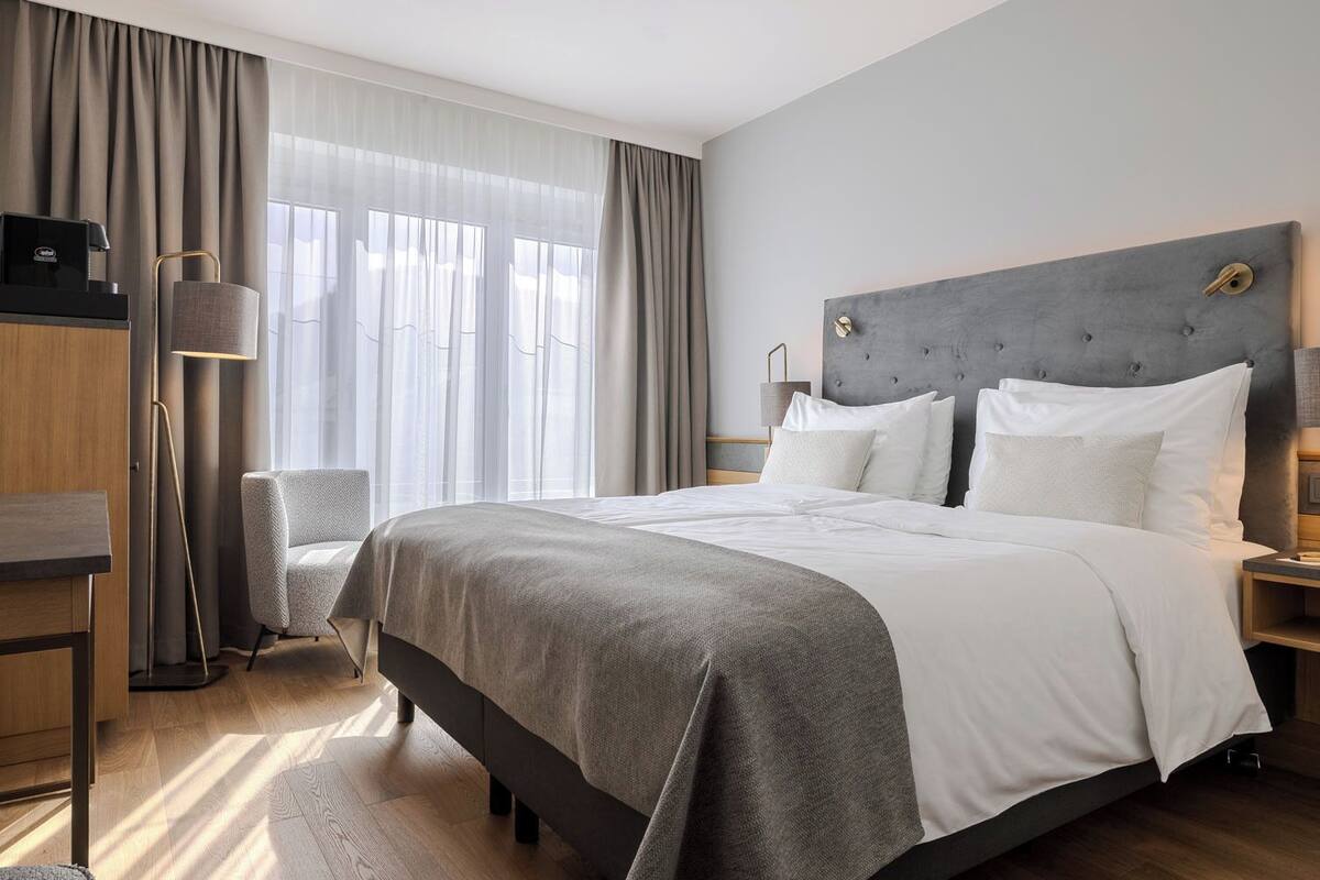 Habitació d'hotel moderna amb un llit gran, una taula de treball, una cadira i una vetustera.