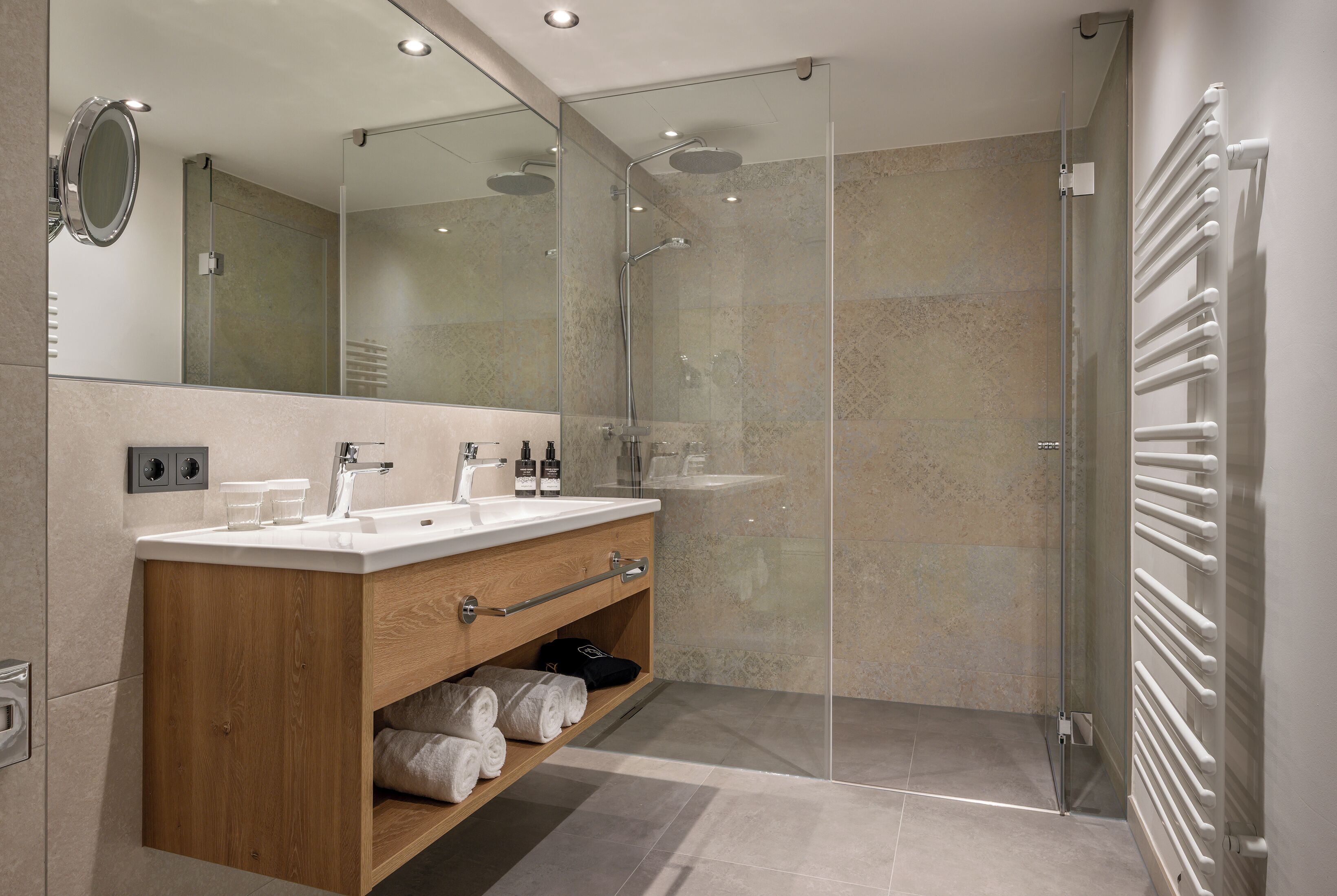 A modern bathroom with a wooden vanity, a glass shower enclosure, and a white towel rack.