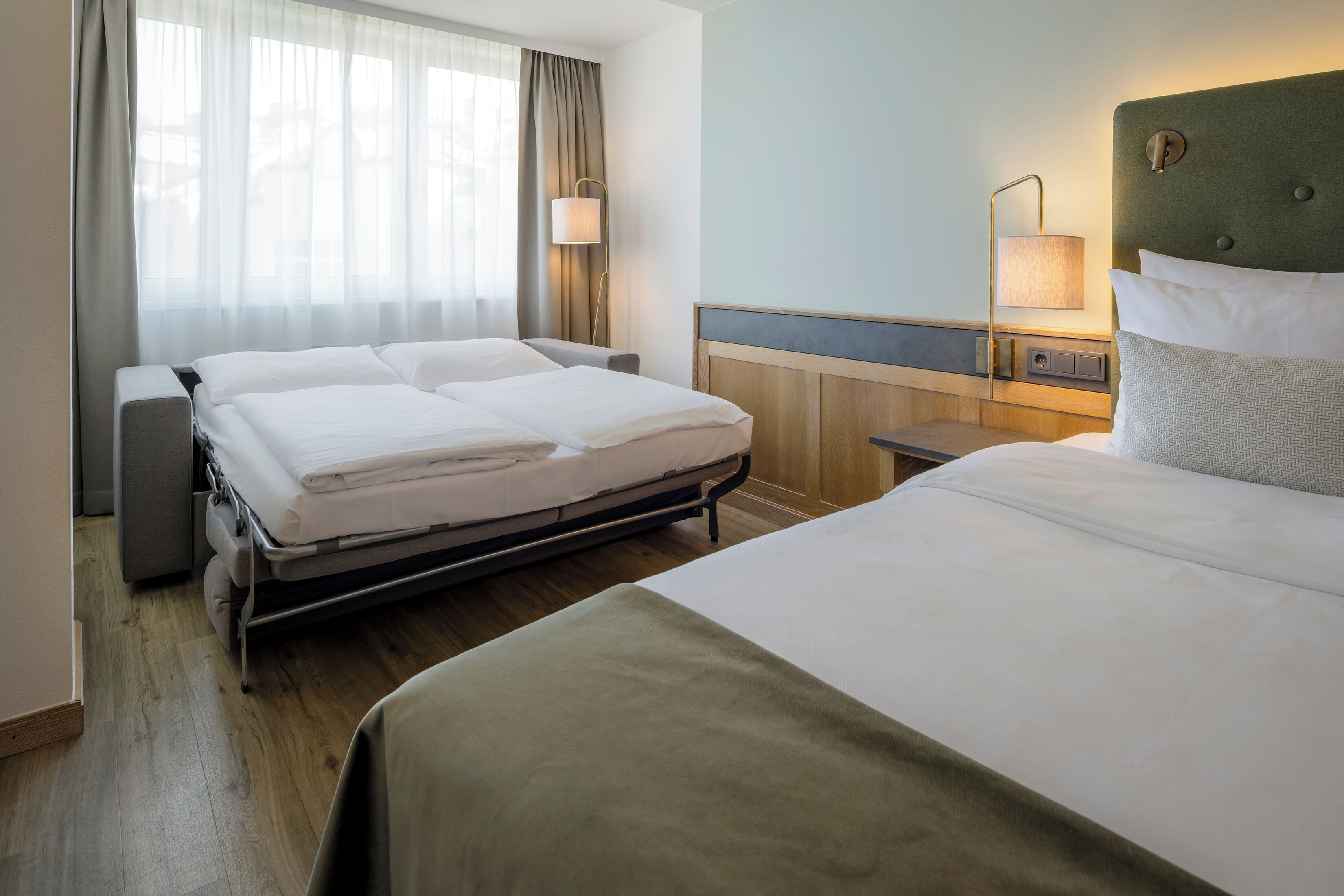 Une chambre d’hôtel avec deux lits, une table de chevet, une lampe et une fenêtre avec des rideaux.