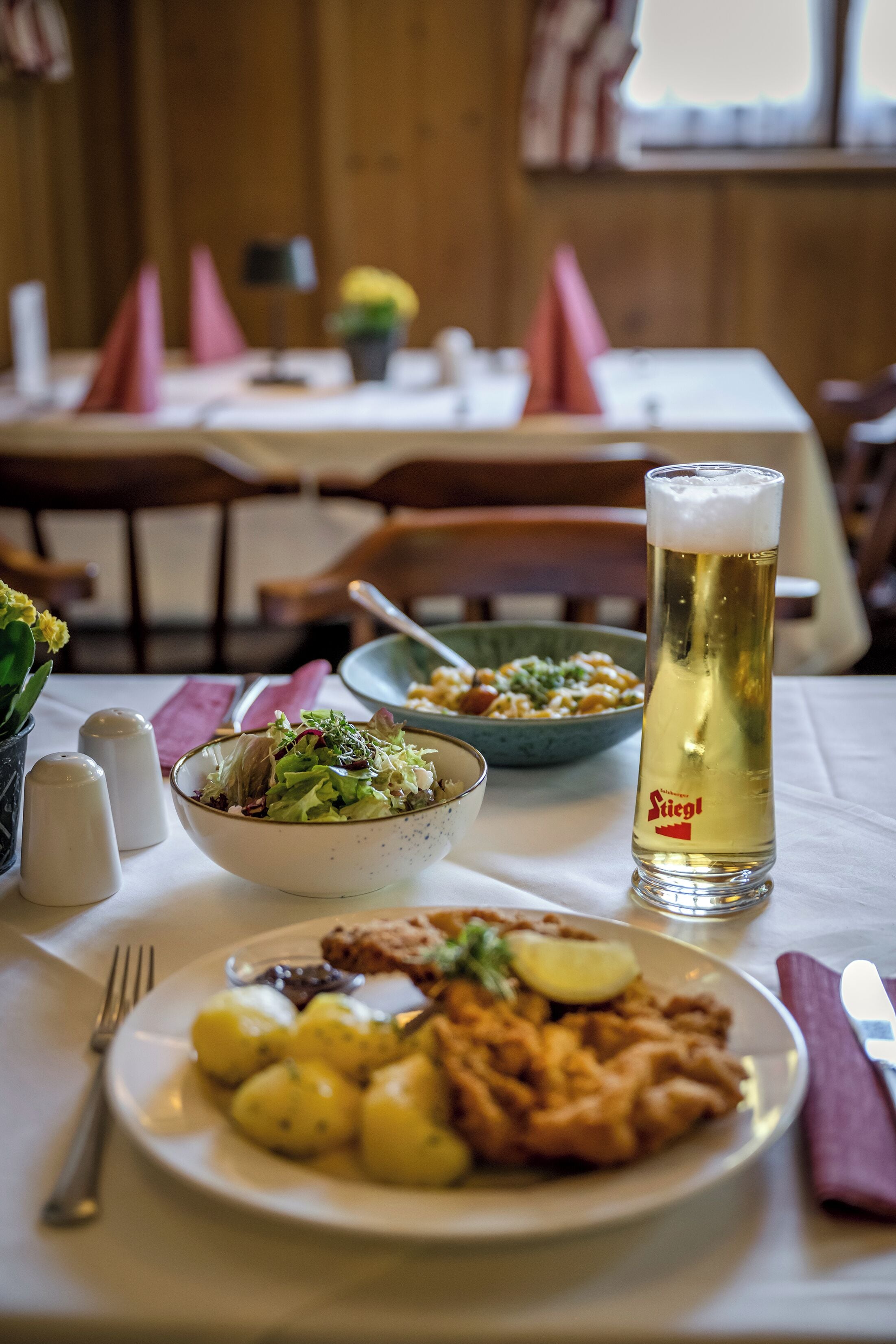 A dining table with a plate of food, a glass of beer, and a bowl of salad.