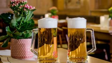 Dos jarras de cerveza sobre una mesa de madera, con una planta en maceta y un recipiente con lunares al fondo.