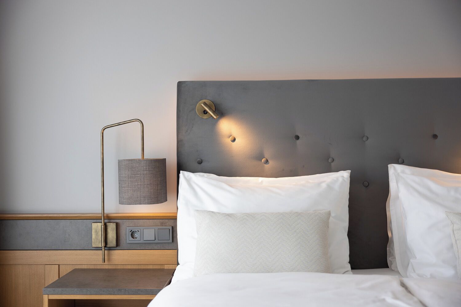 A hotel room with a bed, bedside table, lamp, and a wall-mounted control panel.
