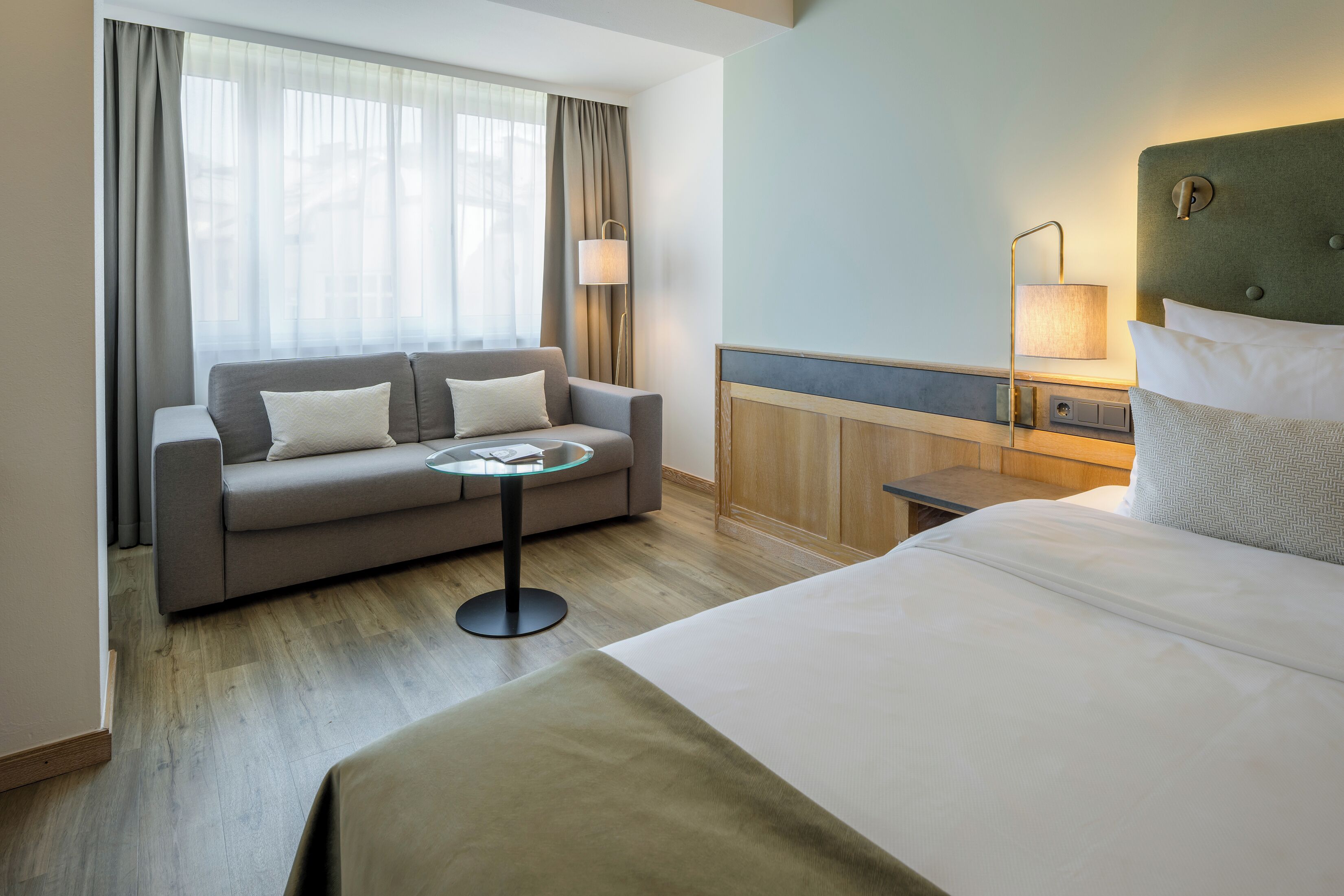 A hotel room with a bed, a sofa, a small table, and a lamp.