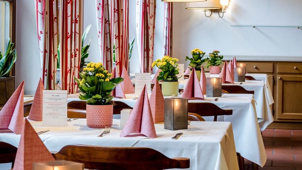 Un restaurant où les tables sont dressées pour le dîner, avec des centres de table illuminés par des bougies et des compositions florales.