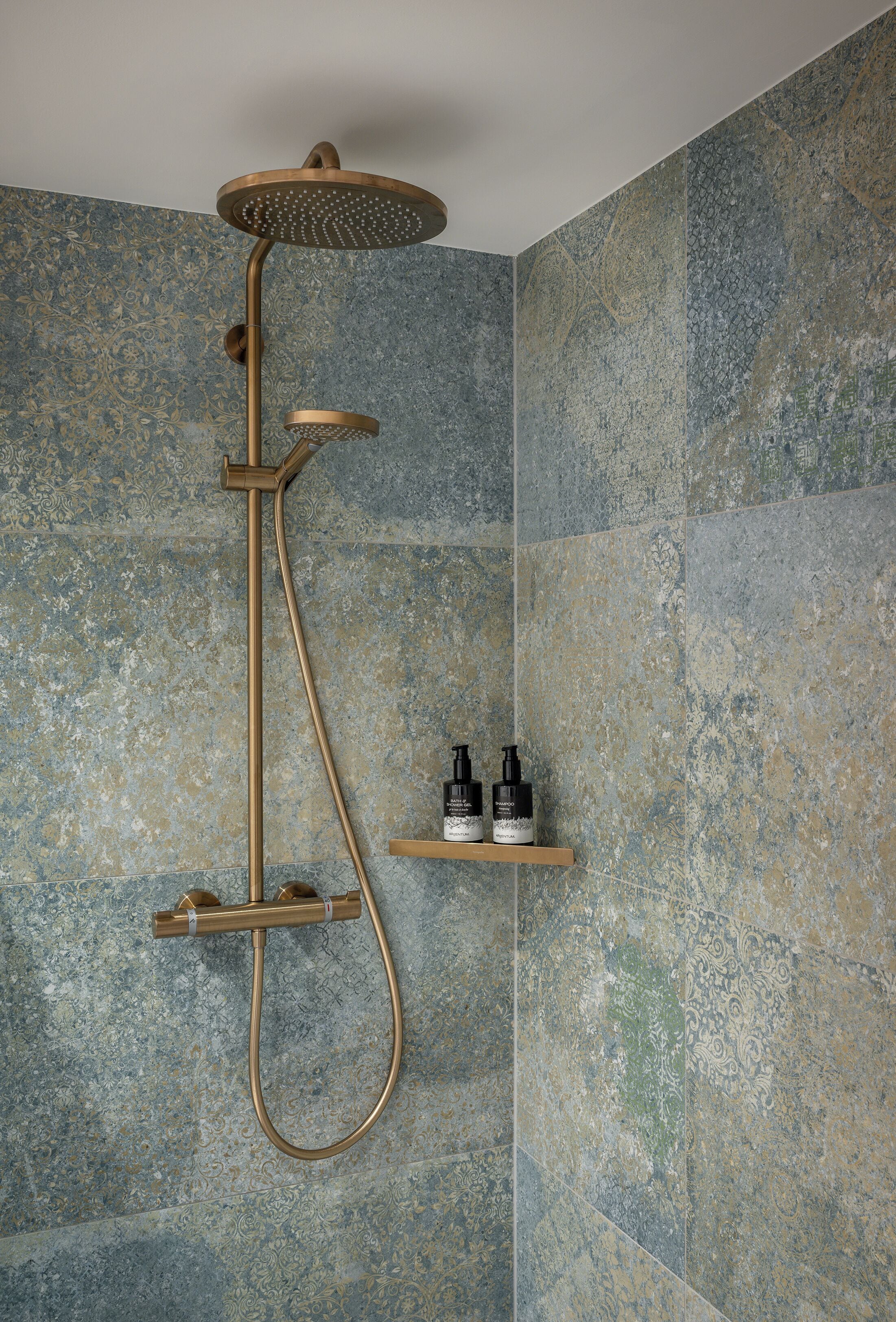 Une douche équipée d’un pommeau de douche à main et d’un système de douche à effet pluie, le tout fixé sur un mur recouvert de carreaux à motifs texturés.