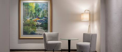 Una habitación con dos sillones grises tapizados, una mesa de vidrio, una lámpara de pie y un cuadro abstracto enmarcado en la pared.