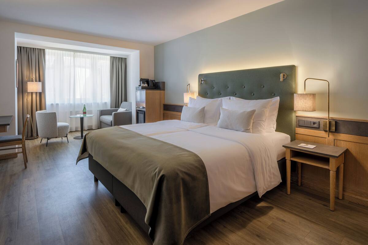 Habitació d'hotel amb un llit gran, escriptori, cadira, làmpada i finestra amb cortines.
