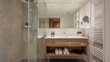 A modern bathroom with a glass-enclosed shower, a wooden vanity with a towel rack, and a built-in shelf for toiletries.
