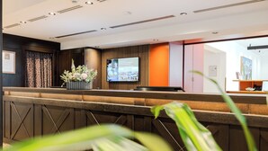 Un espace d’accueil comprenant un comptoir de réception, un écran de télévision et une plante en pot.