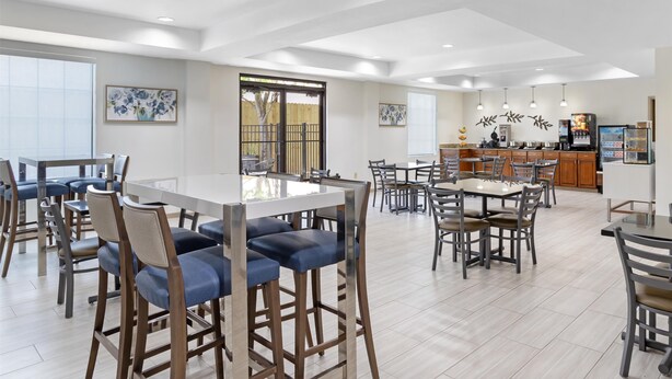 Un grand espace de salle à manger avec des tables et des chaises hautes, un coin cuisine avec un bar, et des œuvres d’art accrochées aux murs.