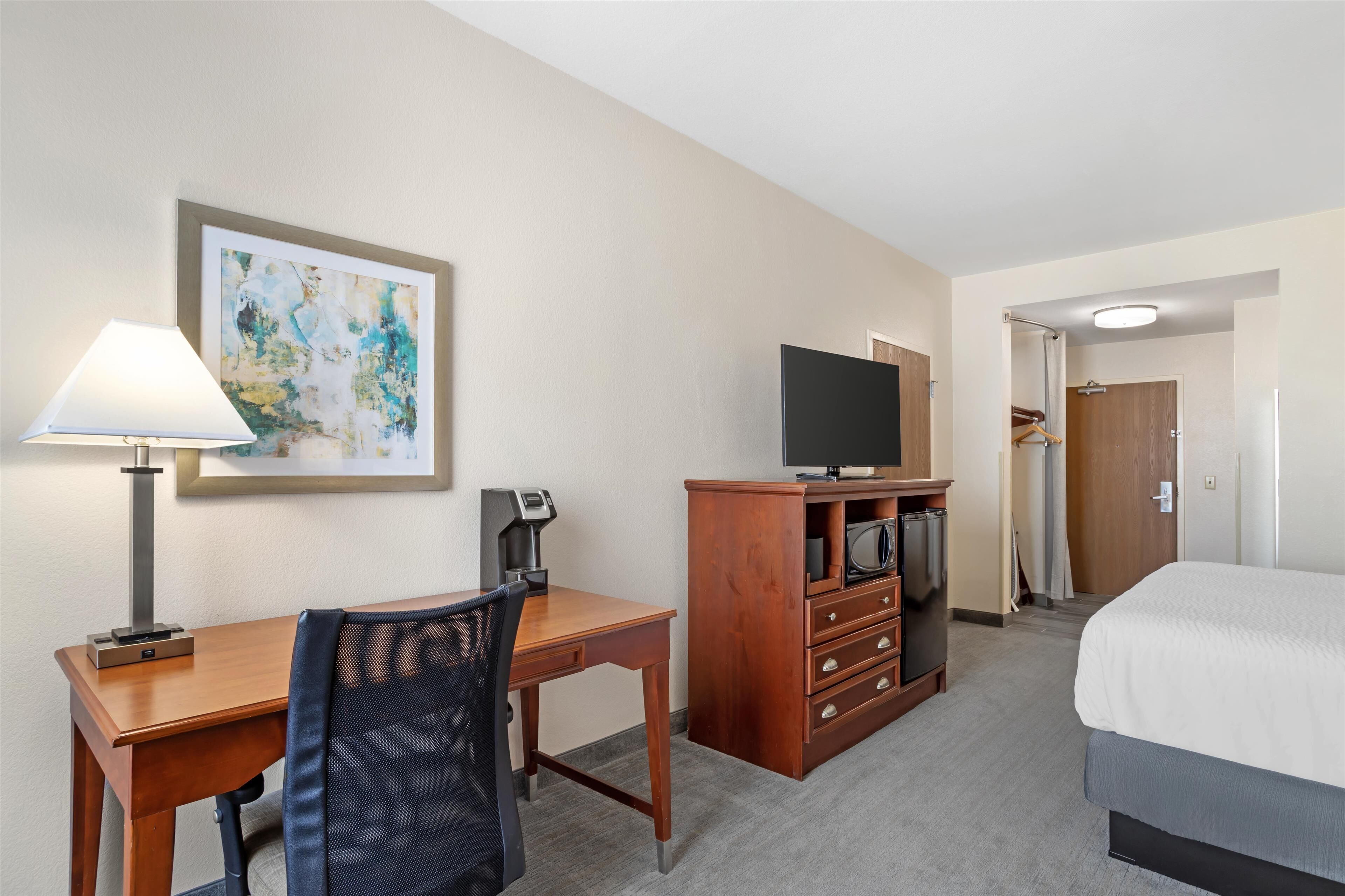 Una habitación de hotel con escritorio, silla, televisor, cómoda y cama.