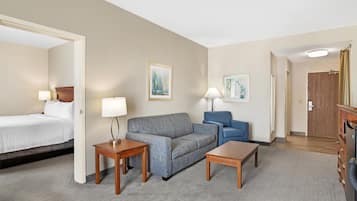A hotel room with a bed, a grey sofa, a blue armchair, two wooden side tables, and a wooden wardrobe.