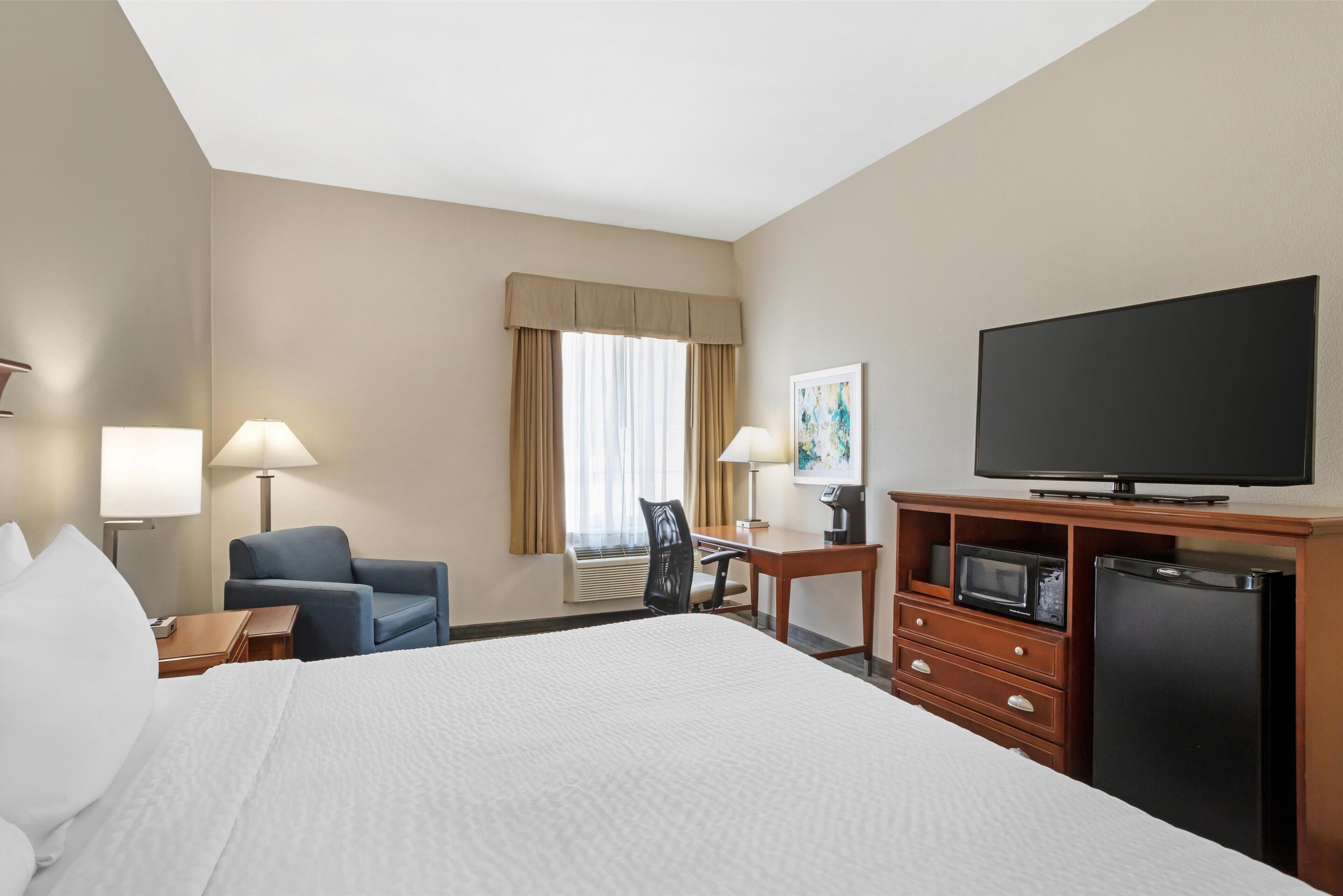 A hotel room with a large bed, two bedside lamps, a desk with a chair, a television, a microwave, and a refrigerator.
