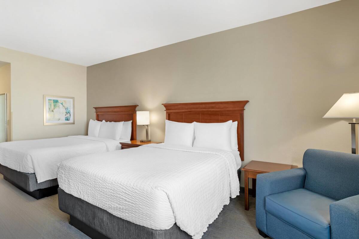 Een hotelkamer met twee bedden, een blauwe fauteuil, een tafeltje en een lamp.