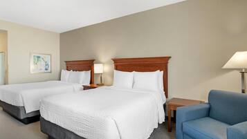 A hotel room with two beds, a blue armchair, a small table, and a lamp.