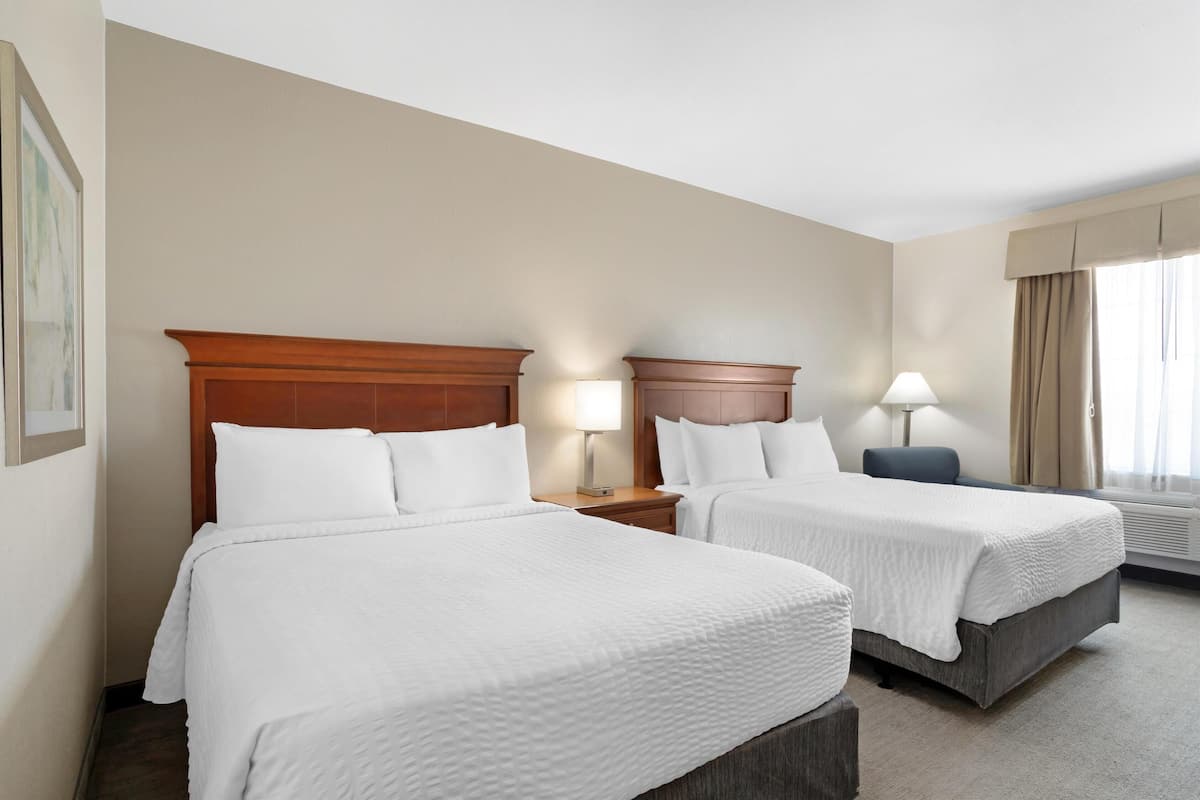 Een hotelkamer met twee bedden, een houten hoofdbord, bedlampjes, een raam met gordijnen en een lijst met een foto aan de muur.