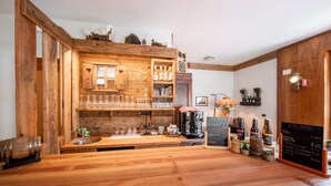 Un coin bar rustique en bois, avec des étagères remplies de verres, une machine à café et un tableau noir servant de menu.