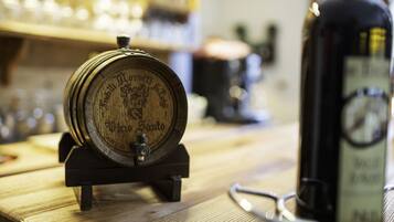 A wooden barrel with a tap on a wooden table, a bottle of wine, and a pair of glasses.