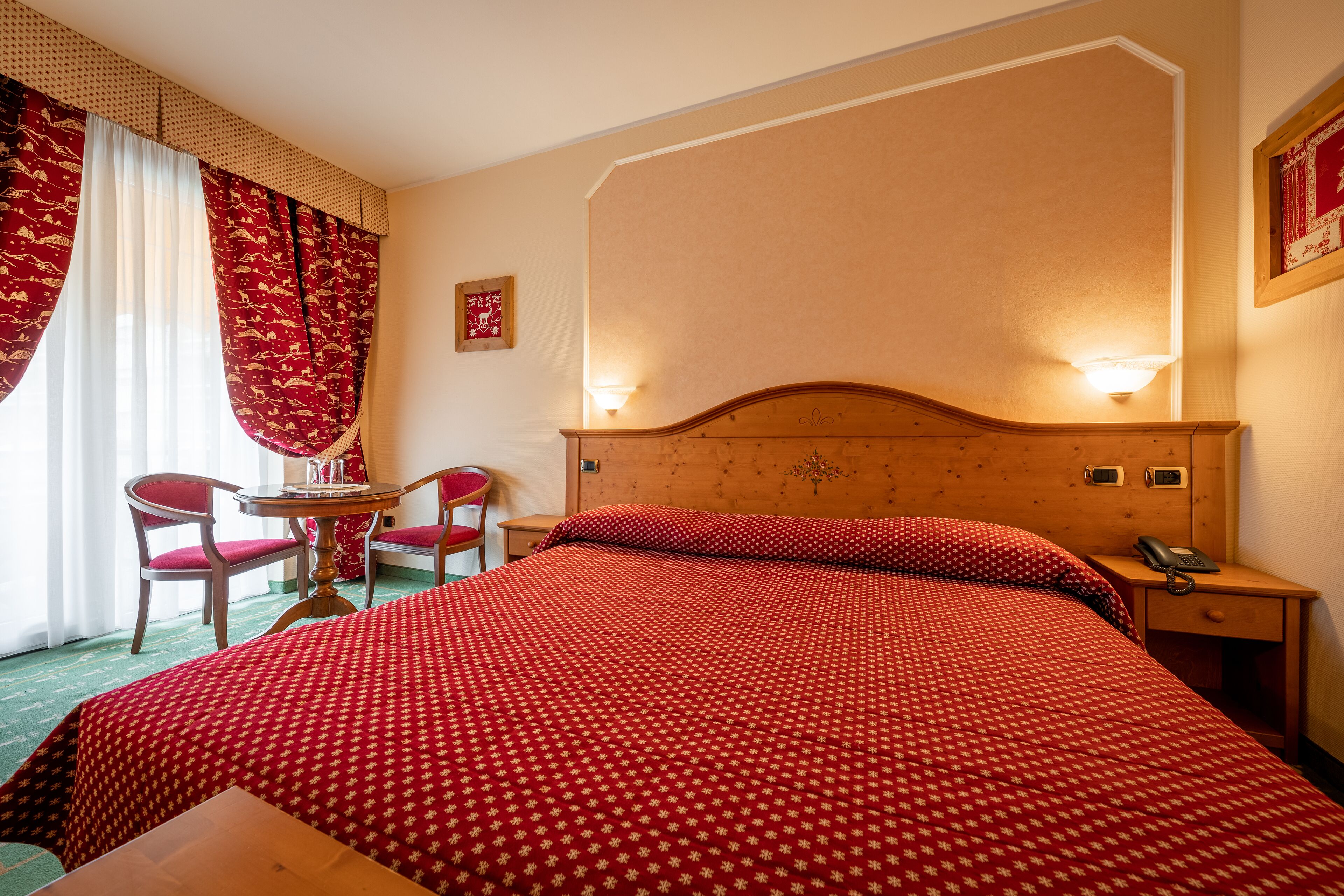 Una habitación de hotel con una cama grande, un cabecero de madera, una mesita de noche con un teléfono y una pequeña mesa con sillas.