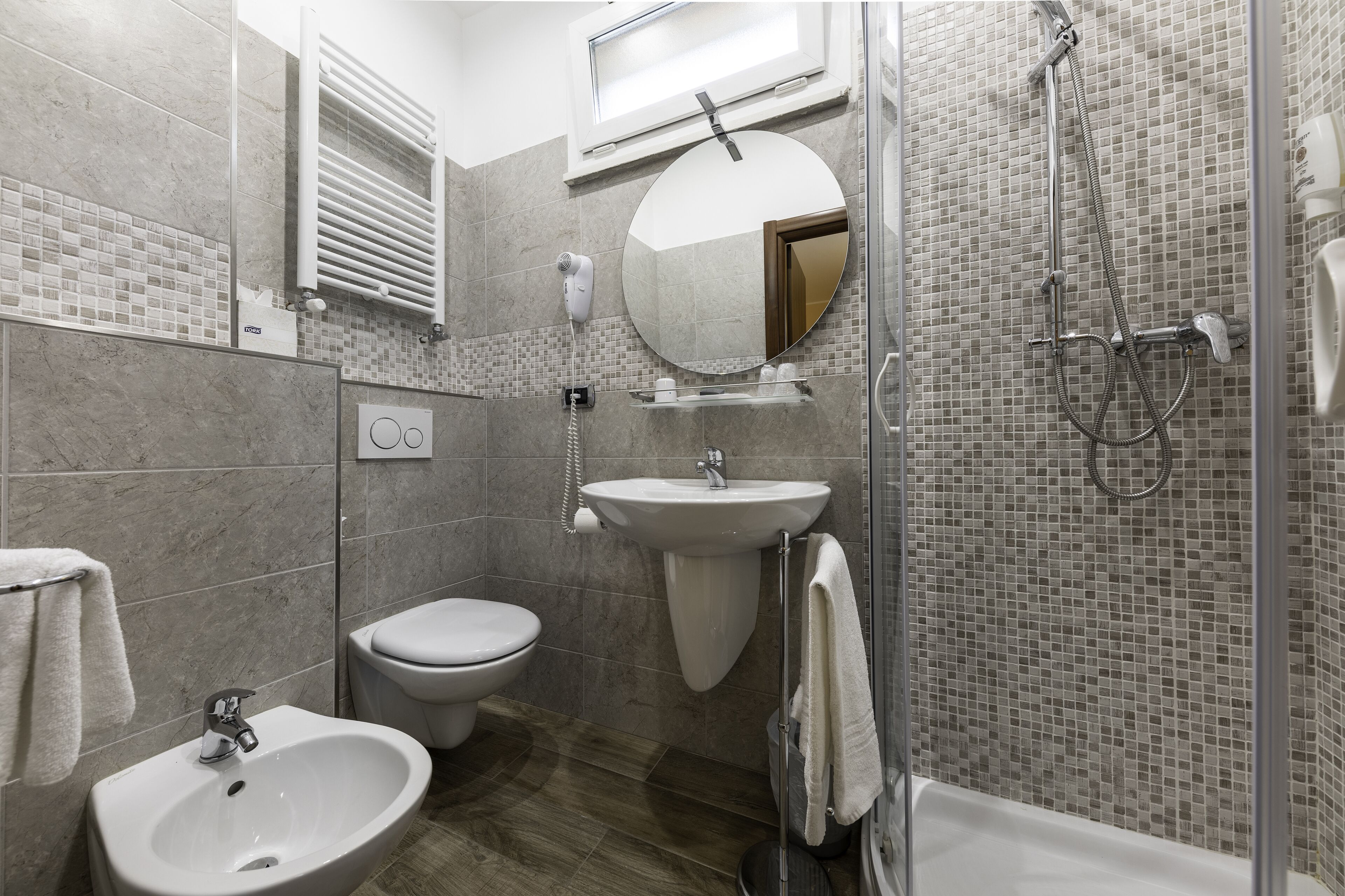 A modern bathroom with a bidet, toilet, sink, and a glass-enclosed shower area.