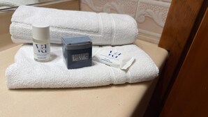 A bathroom counter with a white towel, a bottle of hotel toiletries, a soap bar, and a small packet of soap. - Hotel Le Ville (Capannori)