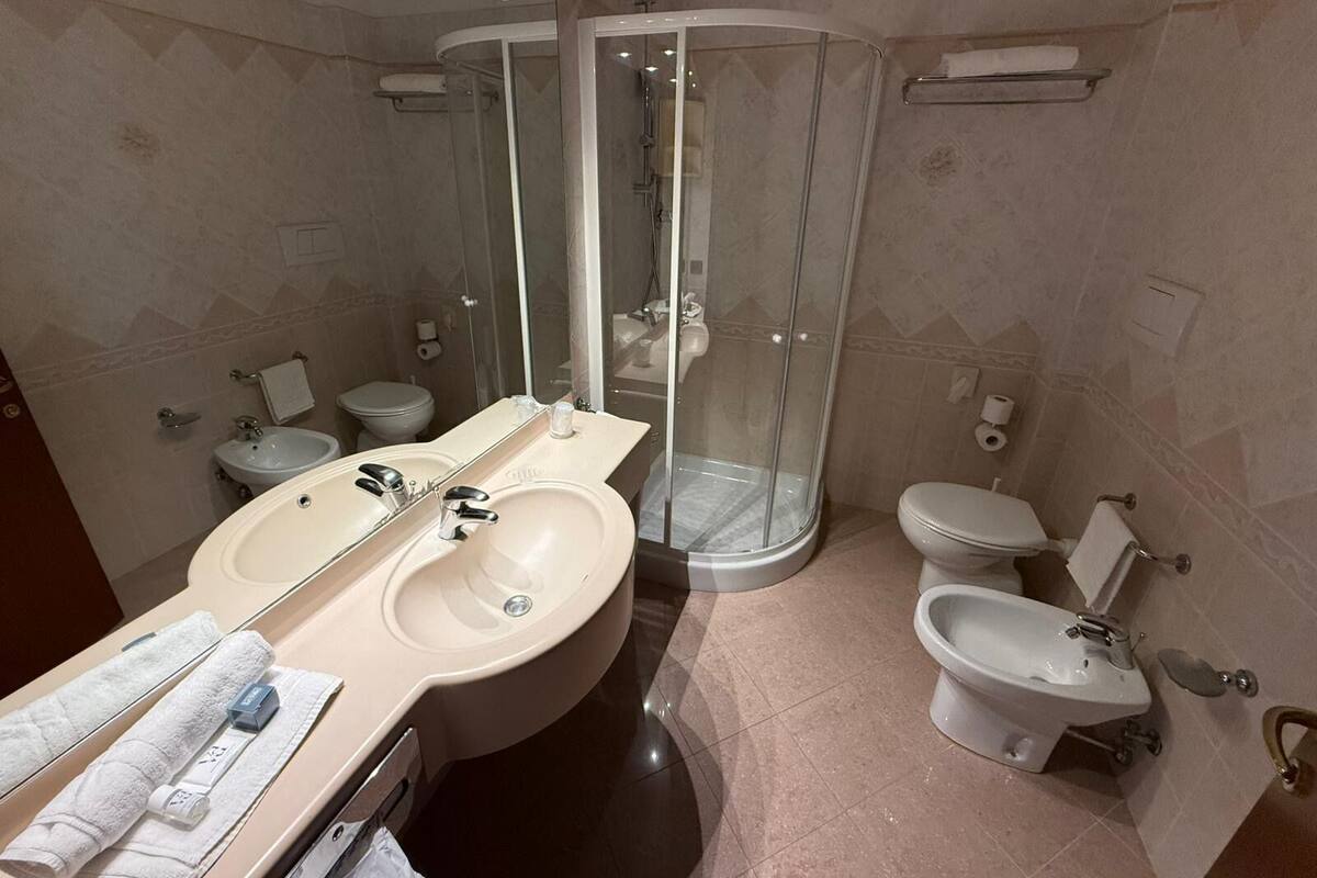 A modern bathroom with a large mirror, two sinks, a shower enclosure, and a toilet.