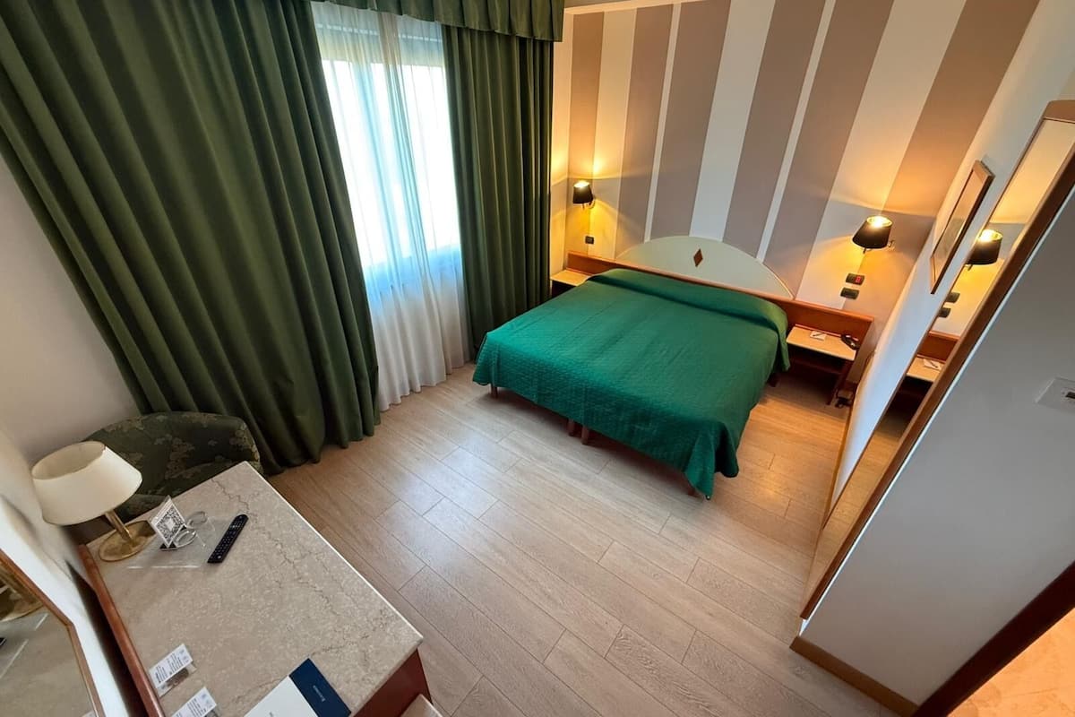 A hotel room with a bed, bedside lamps, a desk with a lamp, and a window with curtains.
