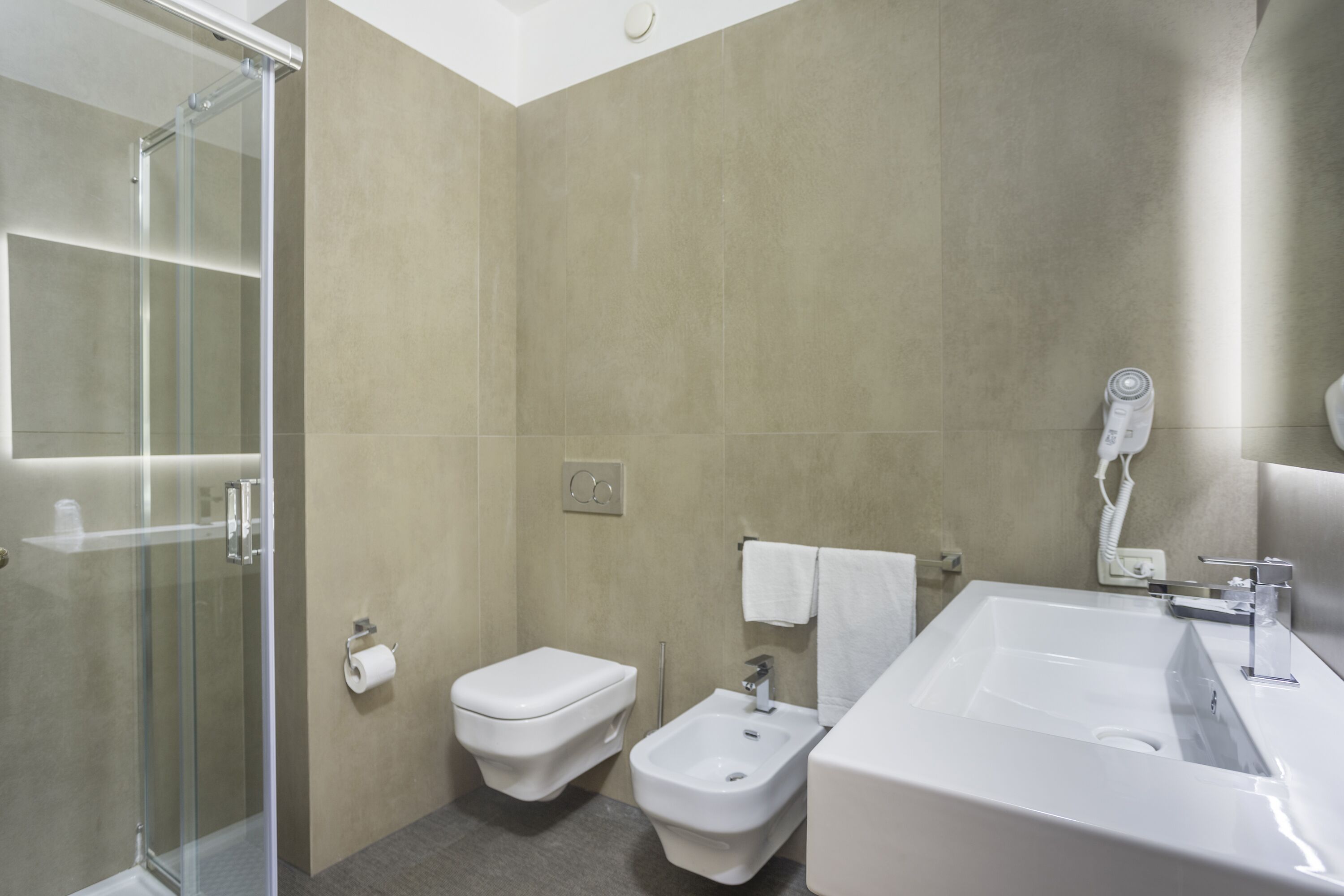 Un baño moderno con cabina de ducha de vidrio, inodoro, bidé y un lavamanos grande con espejo.