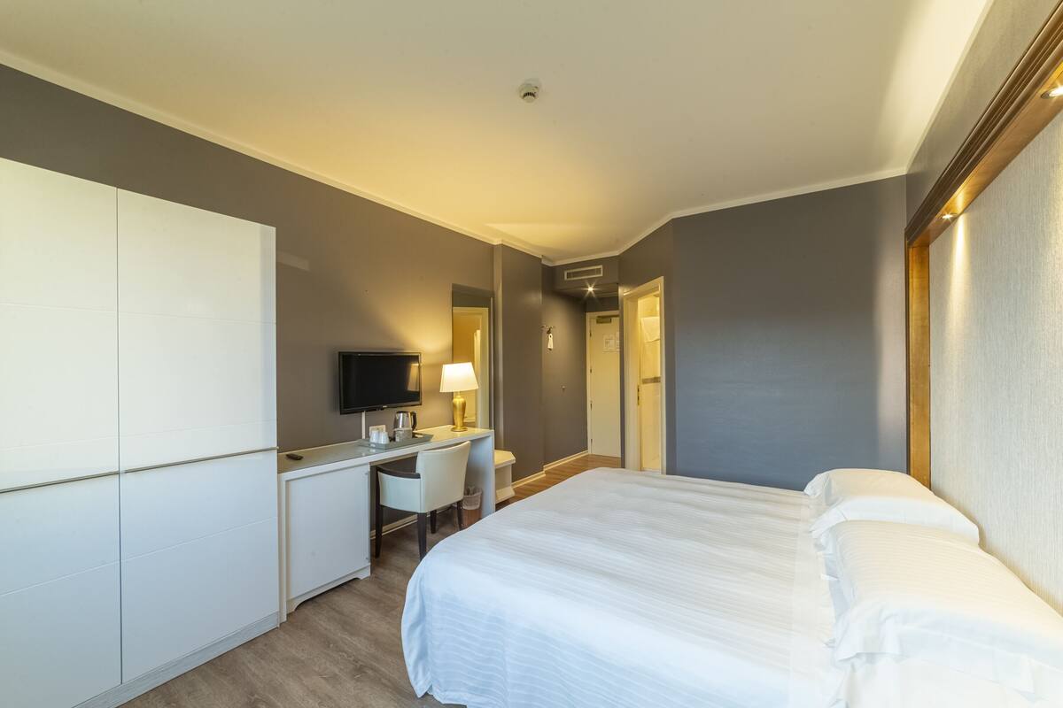 A hotel room with a bed, a desk, a chair, a television, and a lamp.