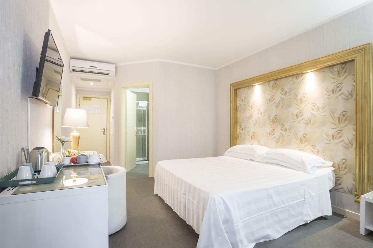 A hotel room with a bed, bedside table, lamp, and a mirror.