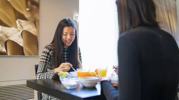 Una mesa de comedor con una persona comiendo, un tazón y un vaso de jugo de naranja.