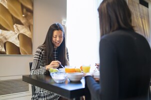Una mesa de comedor con una persona comiendo, un tazón y un vaso de jugo de naranja.