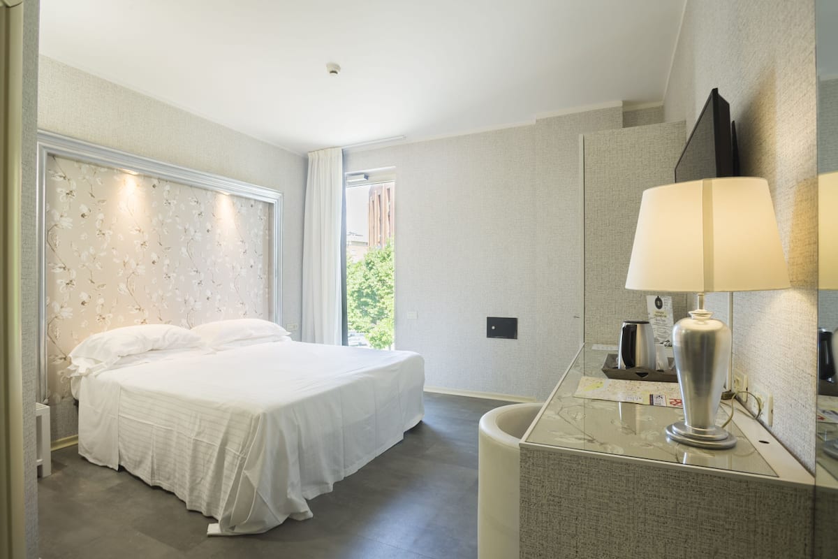 A hotel room with a large bed, a bedside table, a mirror, and a window with curtains.
