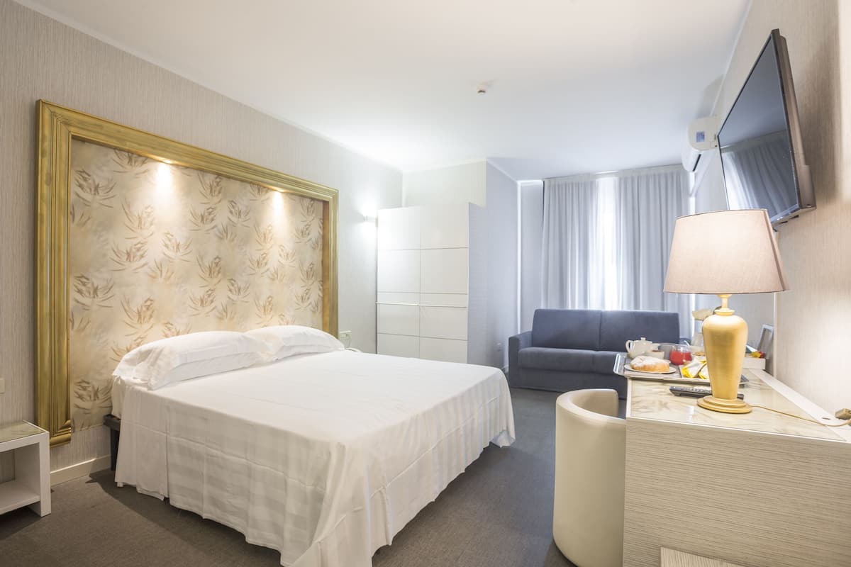 A hotel room with a large bed, a desk with a lamp, a television, and a chair.