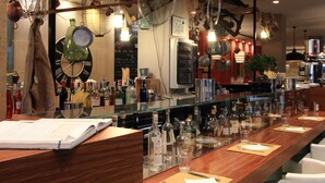 Una zona de bar con una barra de madera larga, varias botellas, vasos y una carta.
