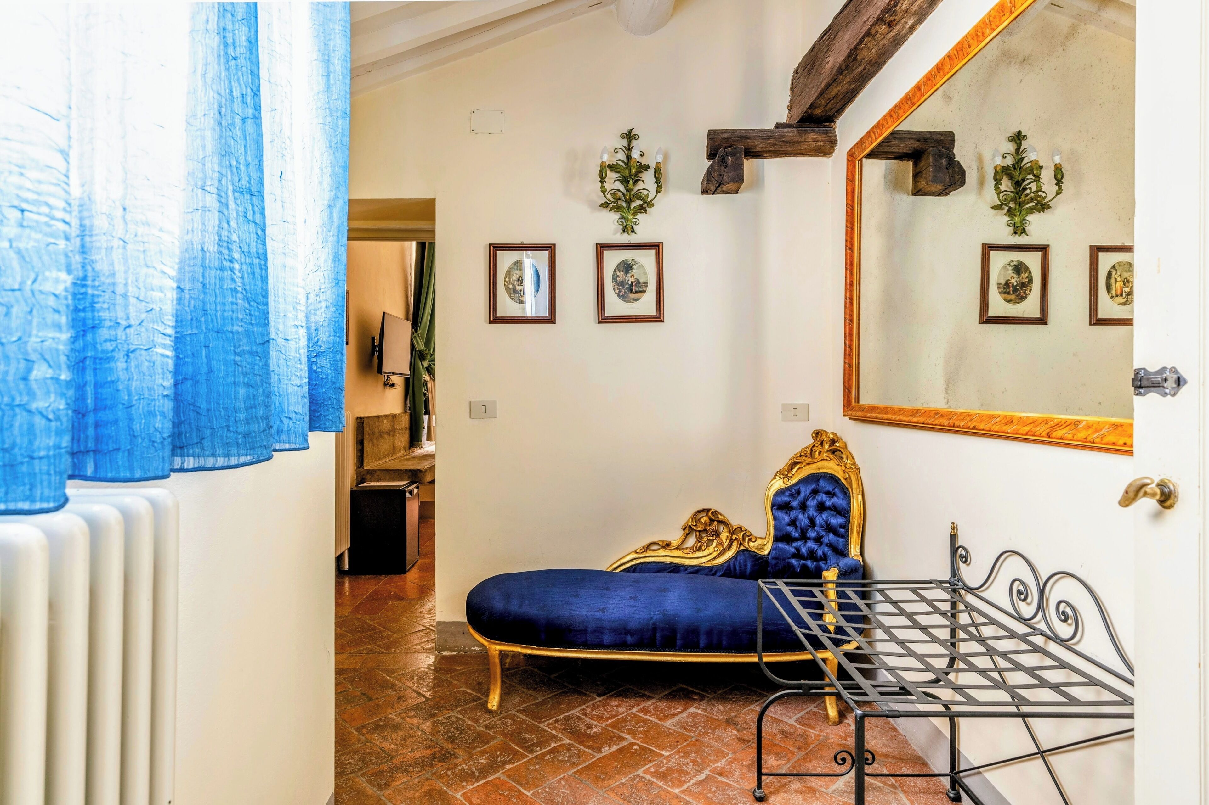 A room with a blue velvet sofa, a metal bed frame, and framed pictures on the wall.