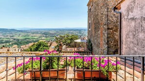 A balcony with terracotta pots of flowers, a view of a rural landscape, and a stone building with a tiled roof. - Hotel San Michele (Cortona)