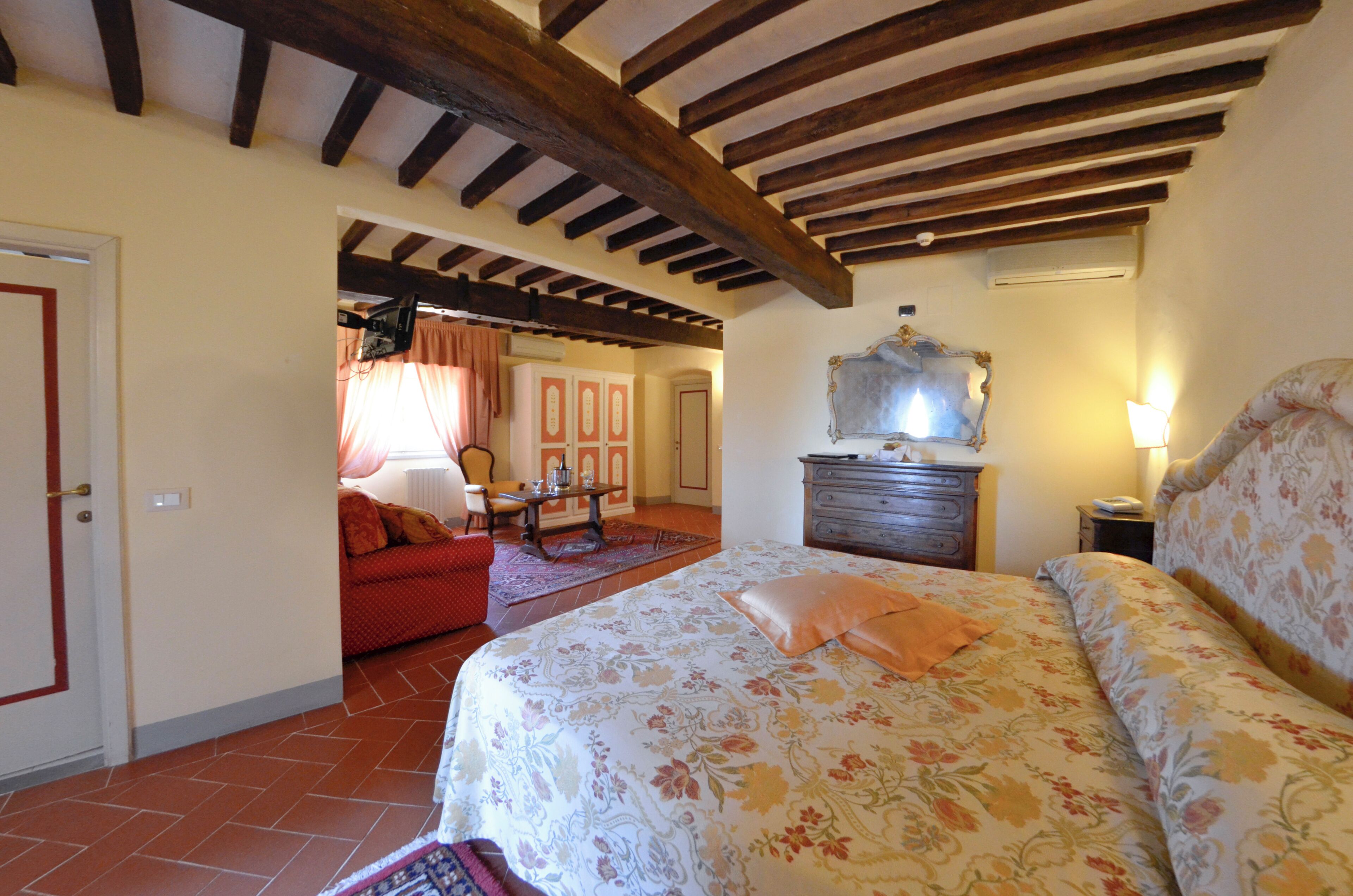 A bedroom with a bed, a dresser, a mirror, and a red sofa in the adjacent room.