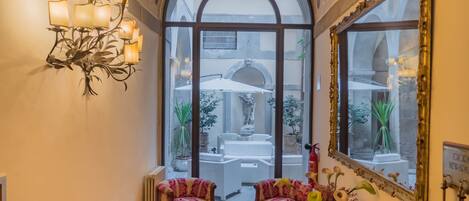 Un couloir avec un tapis à motifs rouges, un lustre, un miroir et une vue sur un espace extérieur aménagé en salon.