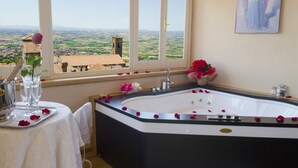 A bathroom with a bathtub, a table with a vase of flowers, and a view of the countryside through a window. - Hotel San Michele (Cortona)