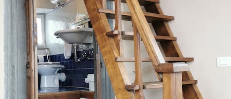 Una escalera de madera que lleva a un baño con un lavamanos y un inodoro a la vista.